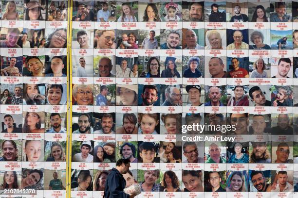 Man passes by a building covered with photos of hostages who have been released or are still being held in the Gaza Strip, on March 26, 2024 in Tel...