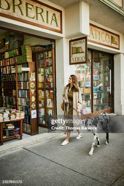 wide shot woman walking great dane past antique bookstore in city - thomas mules stock pictures, royalty-free photos & images