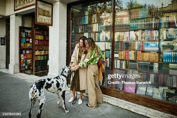 wide shot couple playing with dog while window shopping at bookstore - long coat stock pictures, royalty-free photos & images