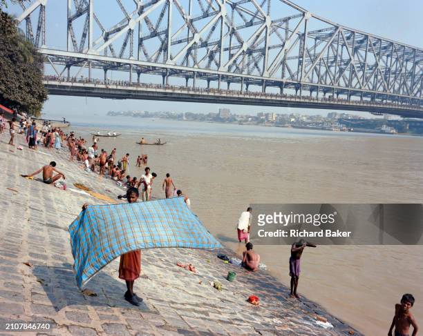 Bathers beneath the Howrah Bridge wash on the banks of the Hooghly River in Kolkata ,18th November 1996, in Kolkata, India. The bridge is one of...