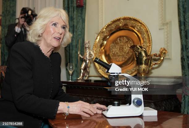 Britain's Queen Camilla looks at a microscope during a reception to mark the findings of a new research study commissioned by The Queen's Reading...