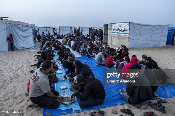 Displaced Palestinians gather to break their fast at a communal table set up amidst the tents as mass iftar dinner organized for displaced...