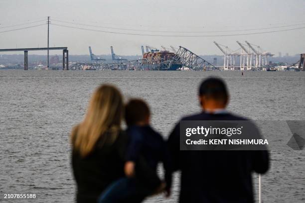 Family looks at the steel frame of the Francis Scott Key Bridge sitting on top of the container ship Dali after the bridge collapsed in Baltimore,...