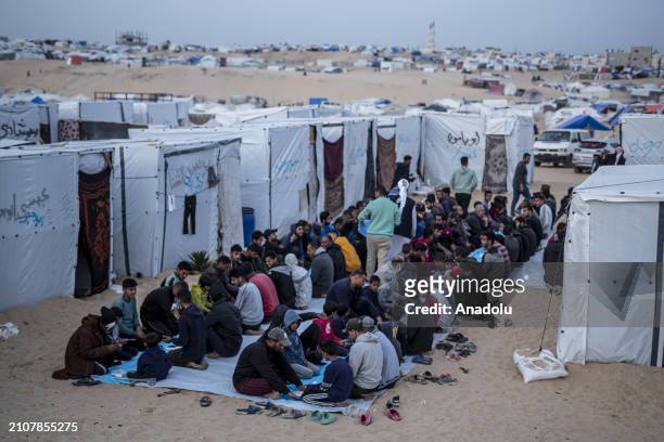 Displaced Palestinians gather to break their fast at a communal table set up amidst the tents as mass iftar dinner organized for displaced...