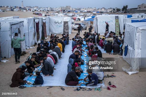 Displaced Palestinians gather to break their fast at a communal table set up amidst the tents as mass iftar dinner organized for displaced...