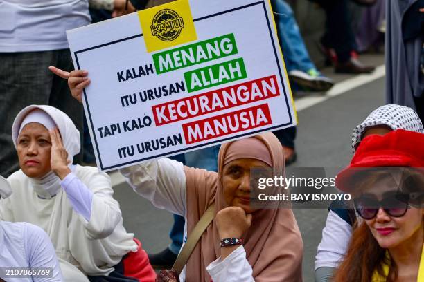 Protestor supporting presidential candidate Anies Rasyid Baswedan shows placard reading "winning or losing is God's business, but cheating is...