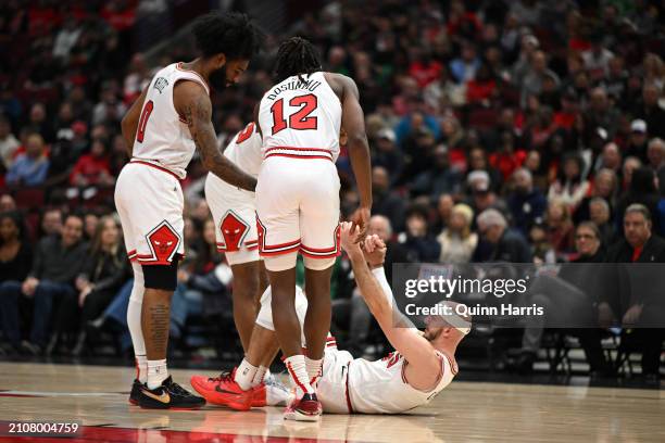 Coby White and Ayo Dosunmu of the Chicago Bulls helps Alex Caruso of the Chicago Bulls to his feet after an apparent injury in the first half against...