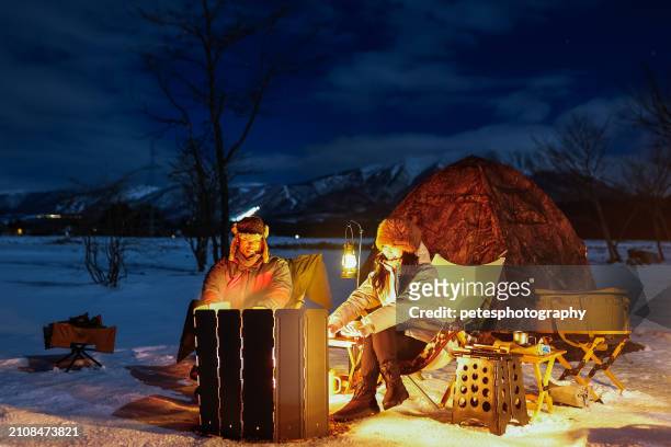 冬のキャンプでキャンプファイヤーのそばでリラックスするカップル - 岩手山 ストックフォトと画像