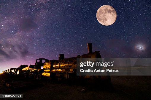 Old locomotive in the train cemetery of Uyuni, Bolivia. Starry night with full moon