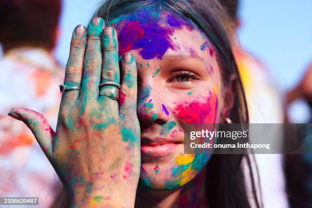 close-up portrait of a joyful blonde girl with hands and face covered in paint at the holi festival, celebrating the holiday. - festival goer stock pictures, royalty-free photos & images