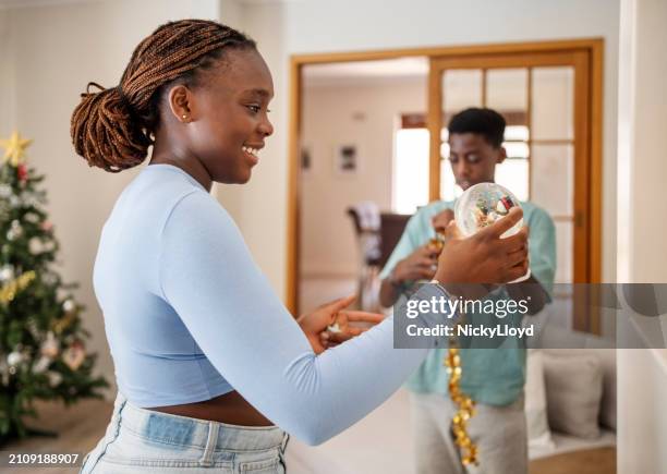 teenager african girl looking at the ornaments while decorating a christmas tree at home - 12 17 months stock pictures, royalty-free photos & images