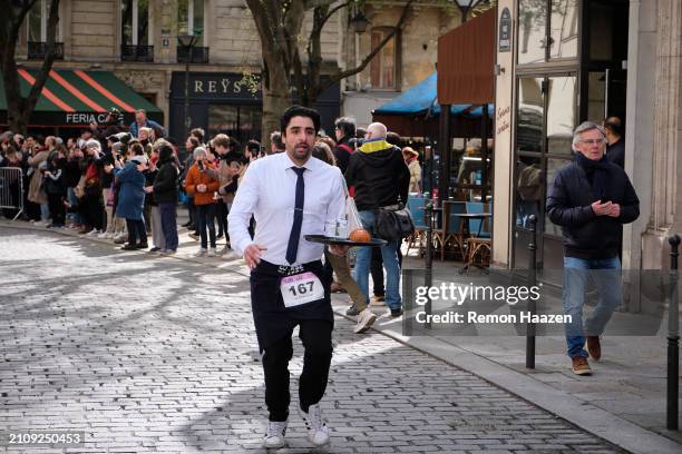 Waiter is seen fast walking holding a tray with drinks and a croissant during the Cafe run on March 24, 2024 in Paris, France. Three hundred waiters...