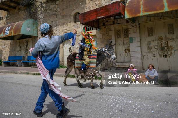 Jewish settler children spray each other with foam wearing costumes celebrate Purim as Israeli security forces secure the celebrations March 24, 2024...