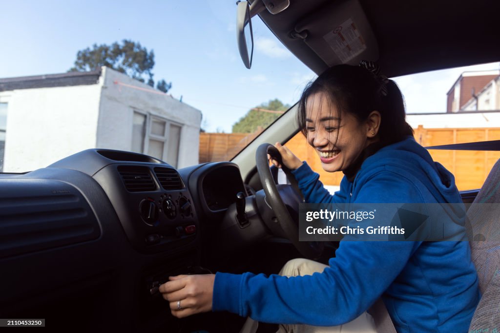 Young adult Southeast Asian Filipino woman prepares for a shopping trip in her car at a residential home driveway in Bristol, England, United Kingdom, Europe