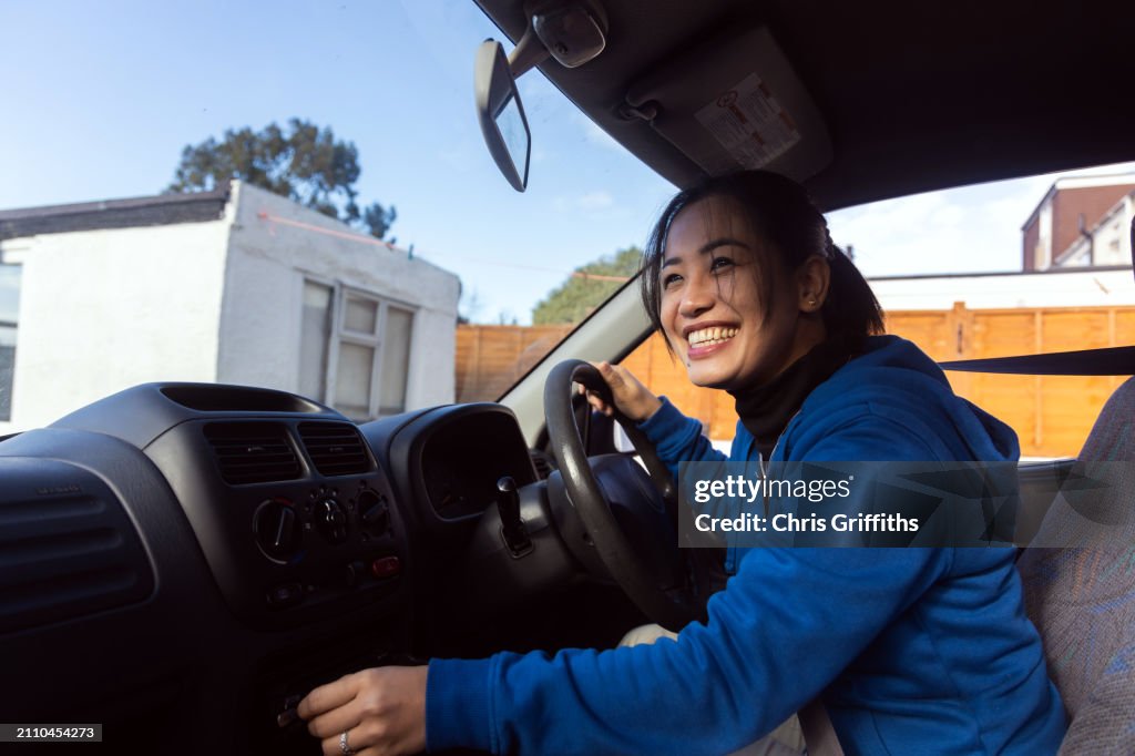 Young adult Southeast Asian Filipino woman prepares for a shopping trip in her car at a residential home driveway in Bristol, England, United Kingdom, Europe