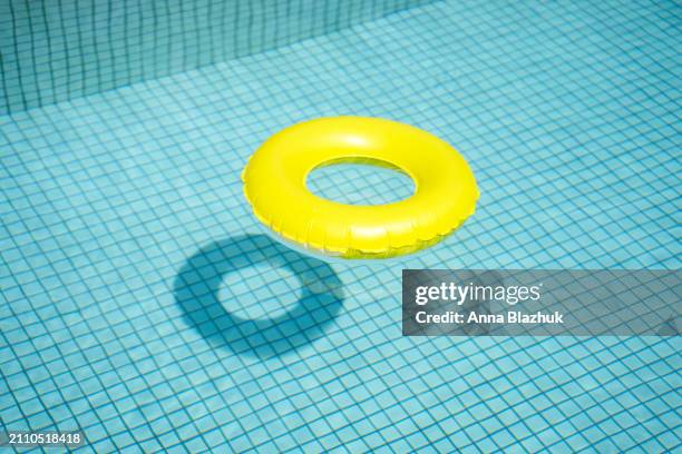 round simple yellow inflatable swim ring in blue pool in bright sunlight. minimalistic summer background. - schwimmring stock-fotos und bilder