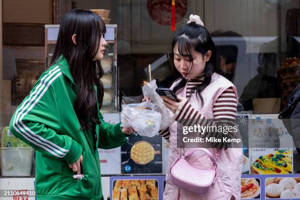 Customers enjoying their snacks and food outside the Chinese Tapas House in Chinatown interacting with their smartphones on 6th March 2024 in London,...