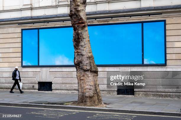 People interacting with a minimal blue billboard sized advertising poster featuring a simple image of a blue sky outside the Garrick Theatre for the...