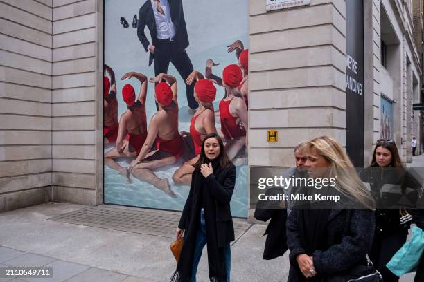 Advertising imagery featuring several women in formation wearing red bathing suits and swimming caps looking up to a male wearing a suit for the...