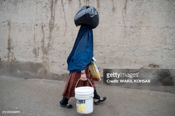 An Afghan burqa-clad woman carrying a plastic bag over her head walks along a street in Kabul on March 27, 2024.