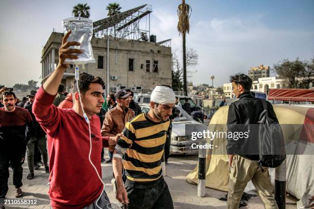 Graphic content / A man assists another to carry an intraveinous solution bag for him as they walk outside the Ahli Arab hospital in Gaza City on...