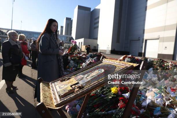 Woman looks at an icon and flowers, laid in front of the Crosus City Hall, destroyed after a terrorist attack, on March 27, 2024 in Krasnororsk,...