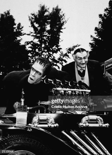 Actors Fred Gwynne and Al Lewis look at a dragster car engine in a still from the television series, 'The Munsters,' circa 1964.