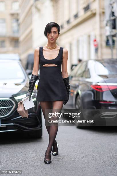 Mollie Chiang wears a Valentino rigid collar, a black sleeveless mini dress with a cut-out at the chest, black leather long gloves, black tights,...