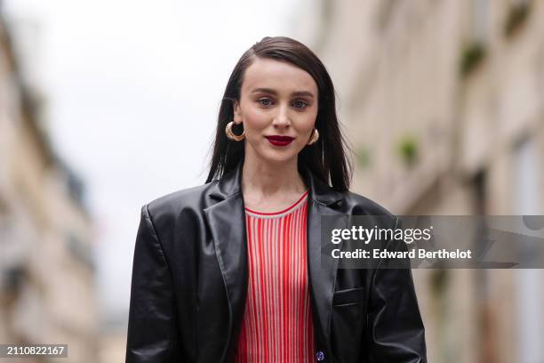 Guest wears earrings, a black leather coat, a dress with red stripes, a white bag, outside Akris, during the Womenswear Fall/Winter 2024/2025 as part...