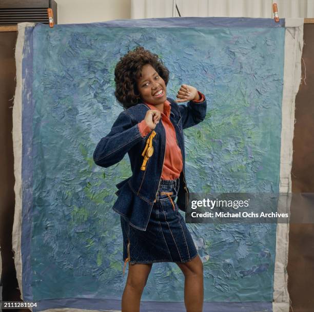 American actress and film director Regina King, wearing a denim jacket with a yellow watch hanging from the pocket, a red shirt and a denim skirt, in...