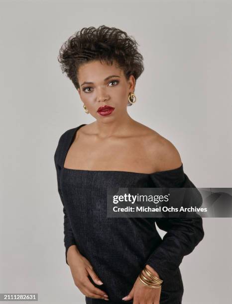 American actress Tisha Campbell, wearing a black minidress, gold hoop earrings and gold bangles, in a studio portrait session, against a white...