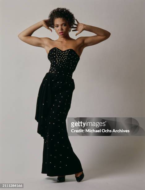 American actress Tisha Campbell, wearing a studded black evening gown with a sweetheart neckline, with her hands behind her head, in a studio...