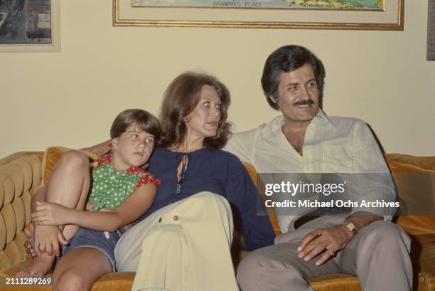 American actress Jennifer Aniston, wearing a red and green polka dot tie-front shirt, sits alongside her parents, American actress Nancy Dow, who...