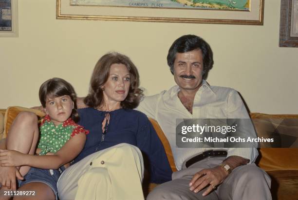 American actress Jennifer Aniston, wearing a red and green polka dot tie-front shirt, sits alongside her parents, American actress Nancy Dow, who...