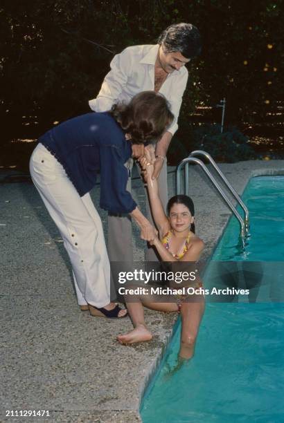 American actress Nancy Dow, wearing a dark blue blouse, embraced by her husband, Greek-born American actor John Aniston, who wears a striped white...