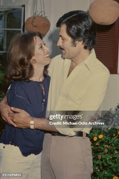 American actress Nancy Dow, wearing a dark blue blouse, embraced by her husband, Greek-born American actor John Aniston, who wears a striped white...