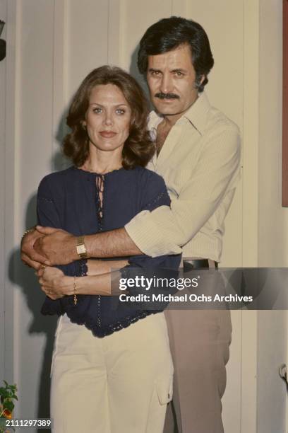 American actress Nancy Dow, wearing a dark blue blouse, embraced by her husband, Greek-born American actor John Aniston, who wears a striped white...