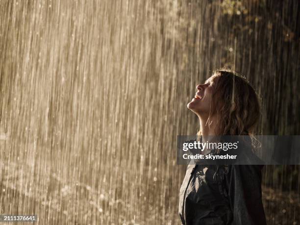 young happy woman in raincoat standing on a rain in nature. - queda de água imagens e fotografias de stock