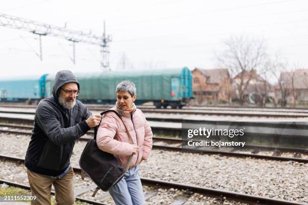 thief in hooded jacket stealing mature woman's laptop bag on train station - mugger stock pictures, royalty-free photos & images