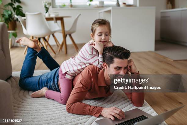 handsome father working from home office, using laptop, daughter helping him, lying on his back. father's day and fatherly love concept. - single father stock pictures, royalty-free photos & images