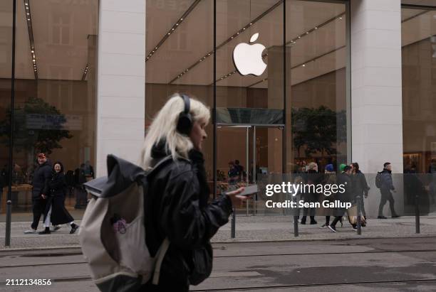 Young woman, who said she did not mind being photographed, wears headphones and holds a smartphone as she walk past an Apple Store on March 25, 2024...