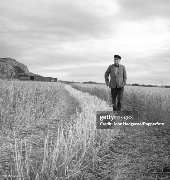 English artist Graham Sutherland walks along a footpath through farmland beside a river estuary near Milford Haven in Pembrokeshire, Wales in 1968.