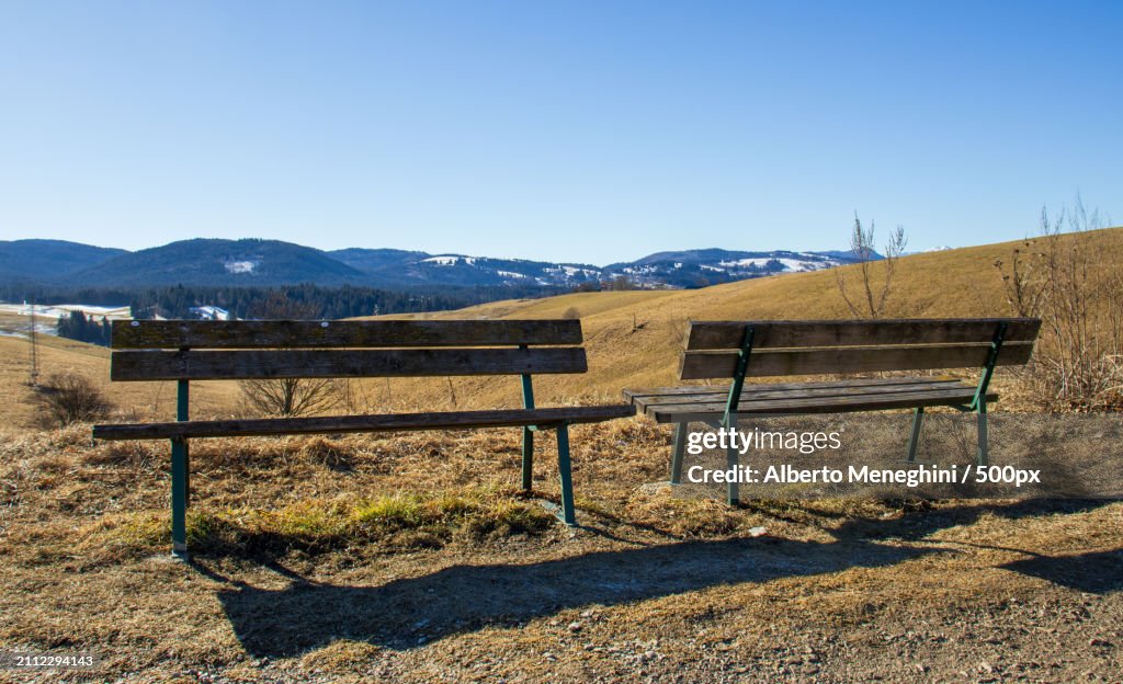 Empty bench on field against clear sky