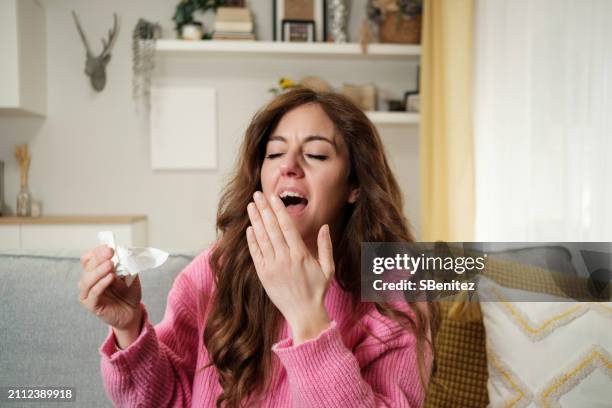 ill woman coughing covering mouth with the hand, sitting on couch - paranasal sinus stock pictures, royalty-free photos & images