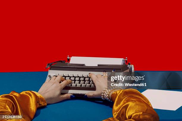 writer typing on typewriter at desk against red background - écrivain photos et images de collection