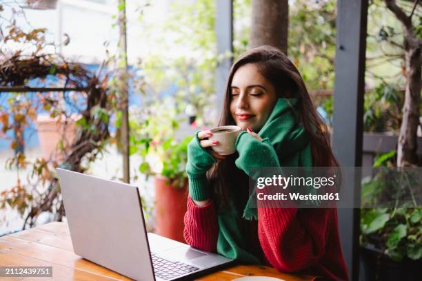 smiling woman enjoying coffee in cafe near laptop - fingerless glove stock pictures, royalty-free photos & images