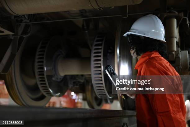 male engineer checking the train parts from below the undercarriage at the railway maintenance workshop - transport ferroviaire photos et images de collection