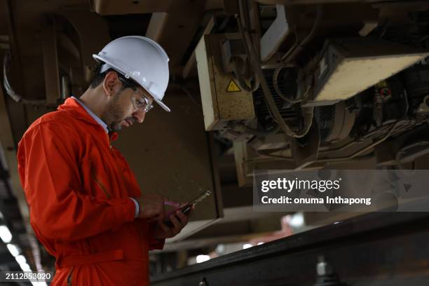 male engineer checking the train parts from below the undercarriage at the railway maintenance workshop - training wheels stock pictures, royalty-free photos & images