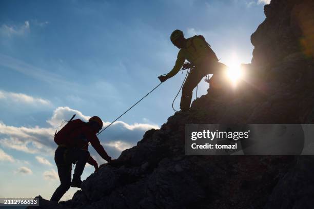 rock climber assisting another - montanhismo imagens e fotografias de stock