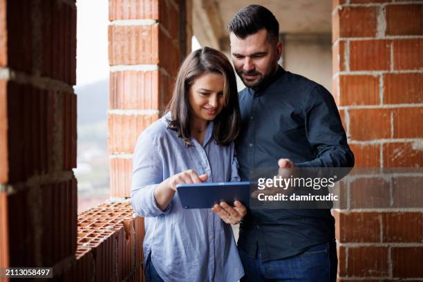 happy couple discussing interior decor ideas using a digital tablet in their new home - bim stock pictures, royalty-free photos & images